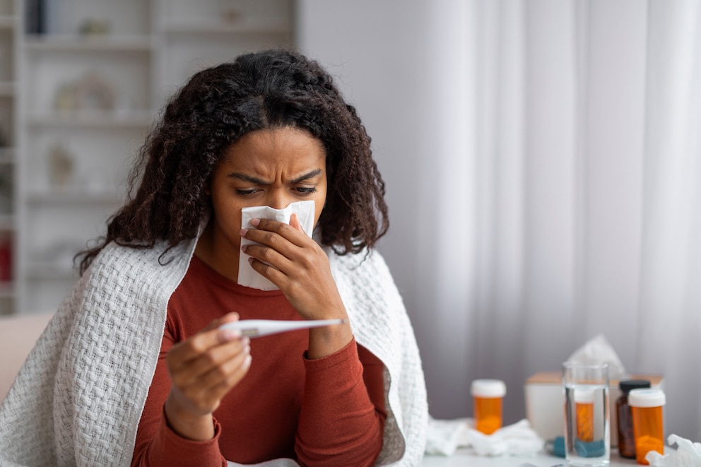 PHOTO: Sick Black Woman Blowing Runny Nose And Looking At Thermometer At Home