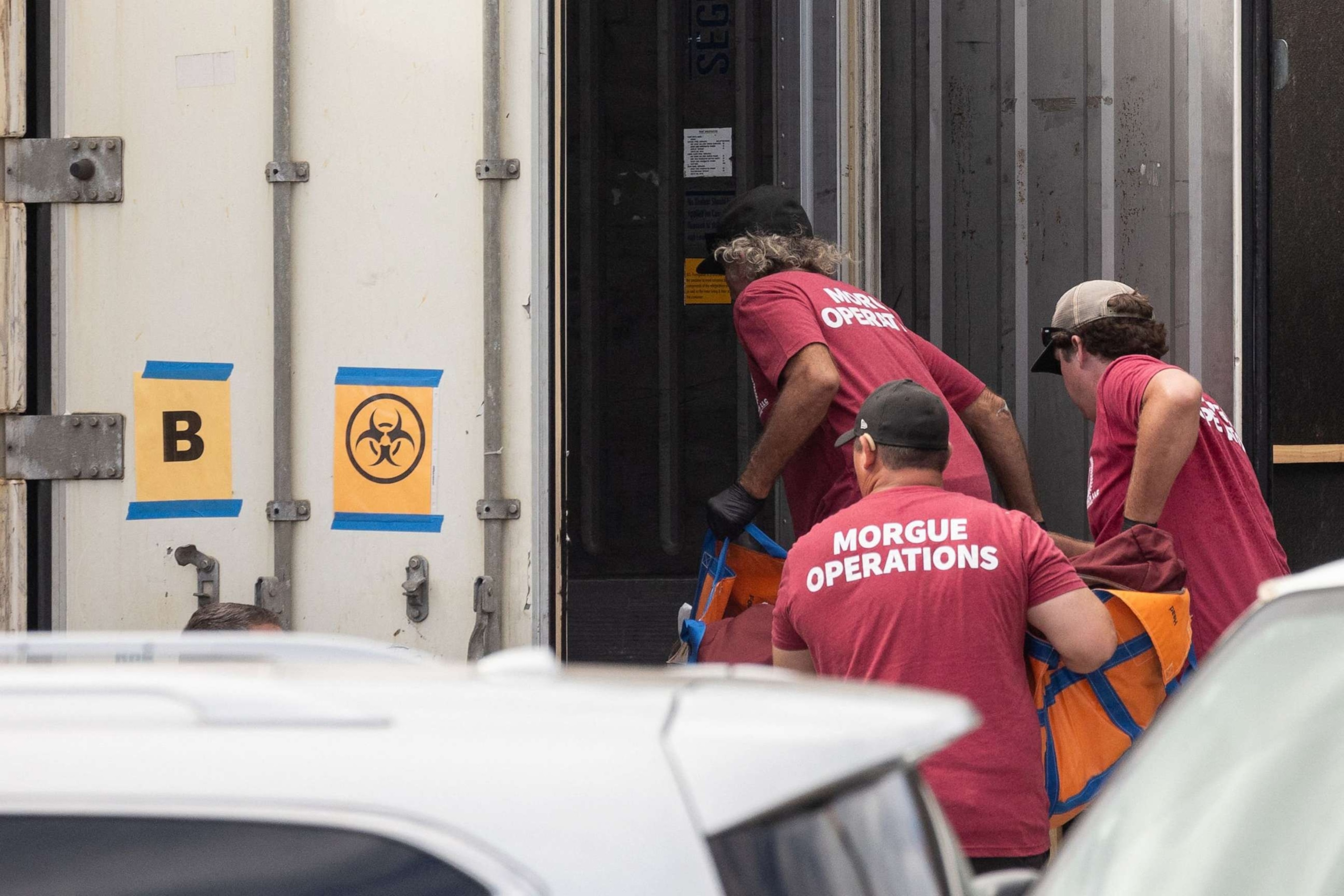 PHOTO: Workers wearing "Morgue Operations" shirts move a body bag into a refrigerated storage container adjacent to the Maui Police Forensic Facility where human remains are stored in the aftermath of the Maui wildfires in Wailuku, Hawaii, Aug. 15, 2023.