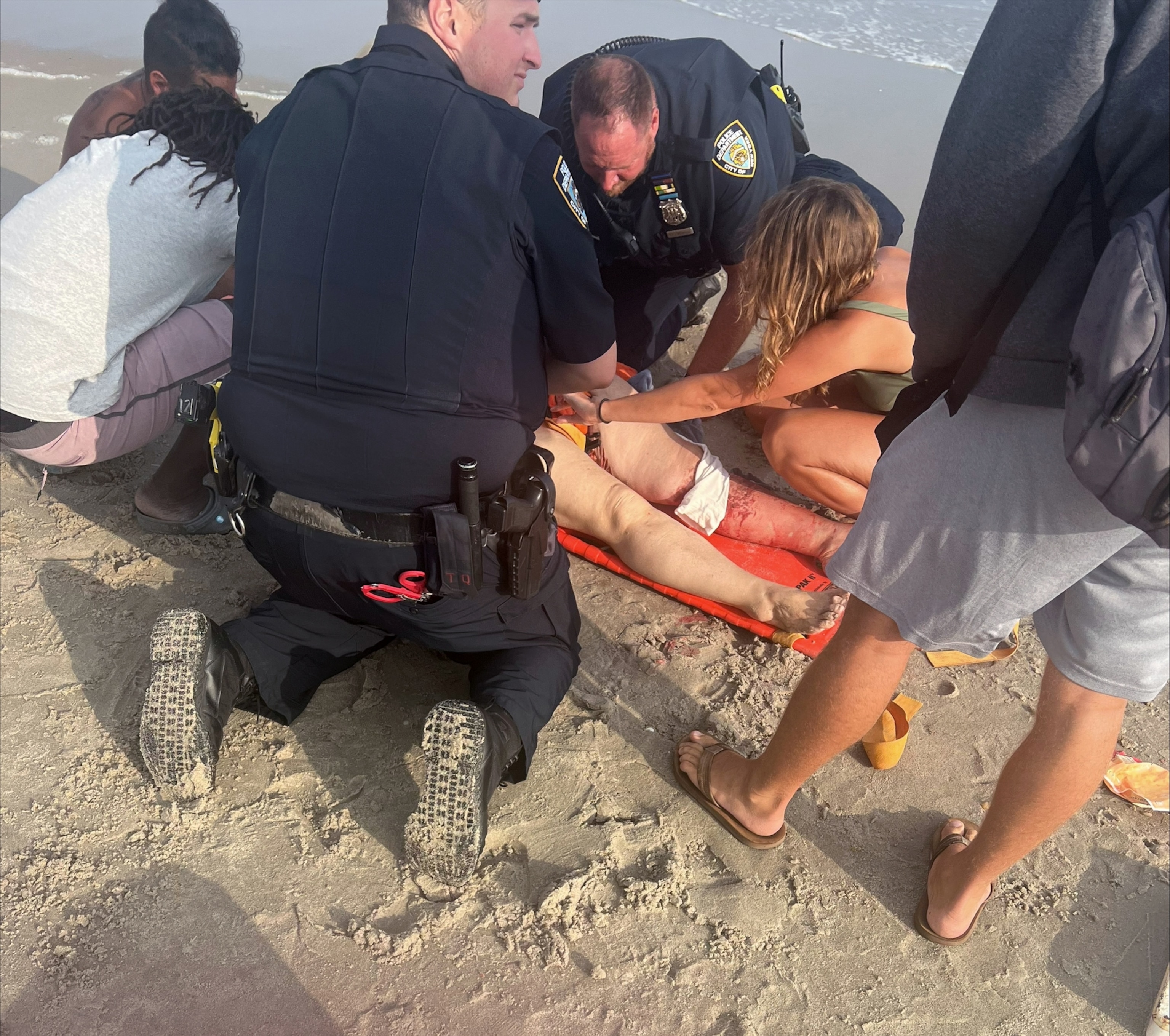 PHOTO: People attend to a 65-year-old woman was bitten by a shark at Rockaway Beach in Queens, New York, Aug. 7, 2023.