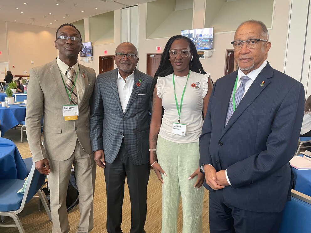 PHOTO: Four people pose in a conference room, wearing business attire with name tags and lanyards.
