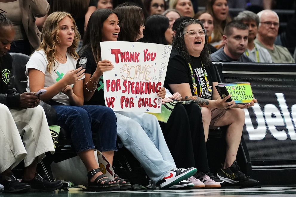 PHOTO: A fan holds a sign for Indiana Fever guard Sophie Cunningham in reference to her comments on transgender athletes as a fan holds a competing sign during the first half of a WNBA basketball game, July 28, 2026, in Seattle.