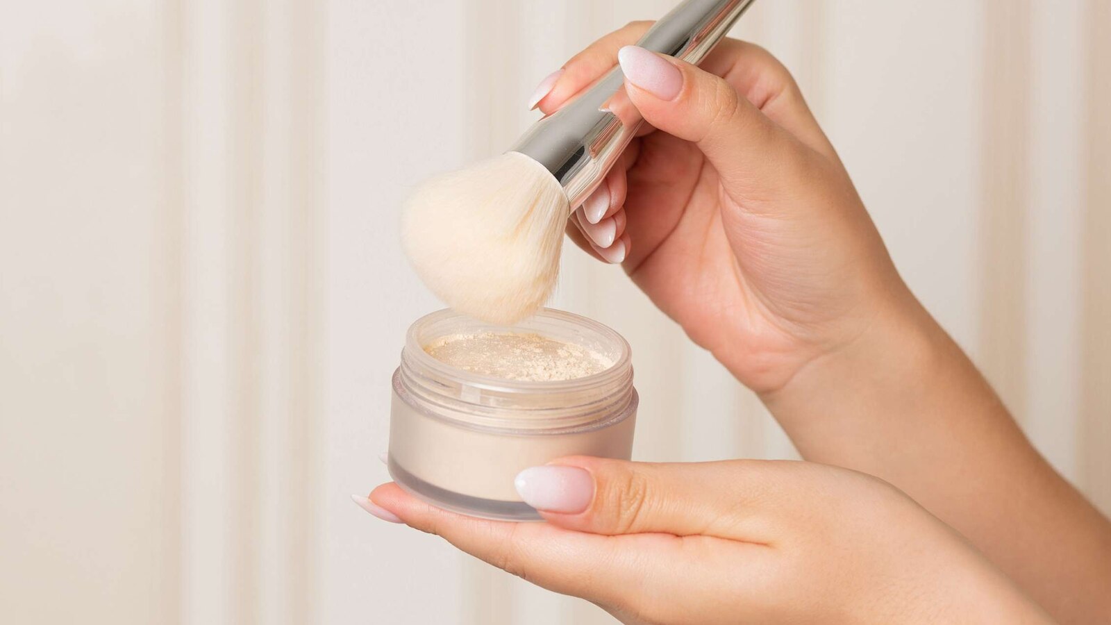 In an undated stock photo, a woman holds a brush and setting powder against a beige background.