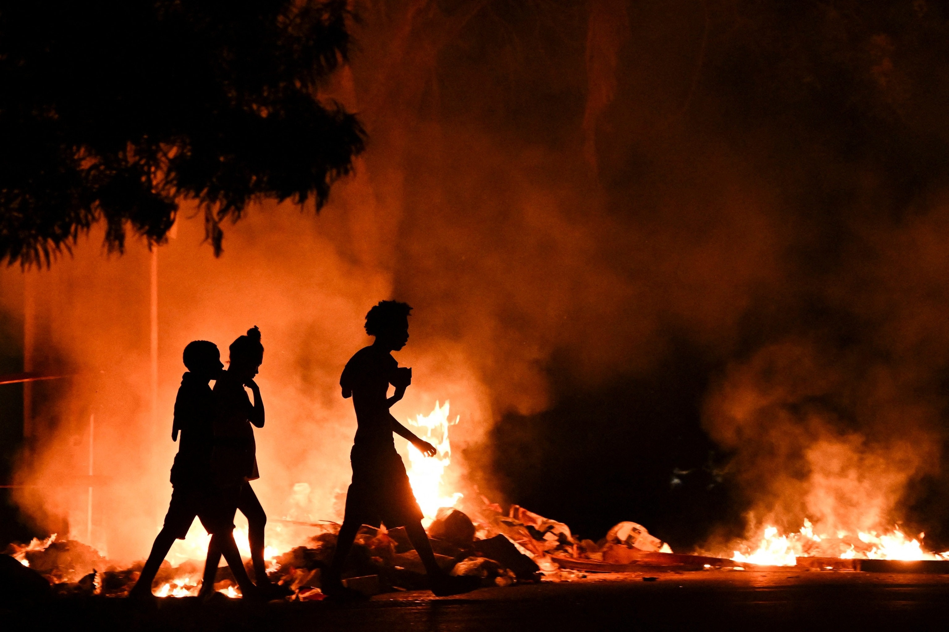 FOTO: La gente pasa junto a un incendio provocado por manifestantes durante una manifestación contra la falta de energía y los cortes de energía en el barrio Lawton de La Habana, el 14 de mayo de 2026.