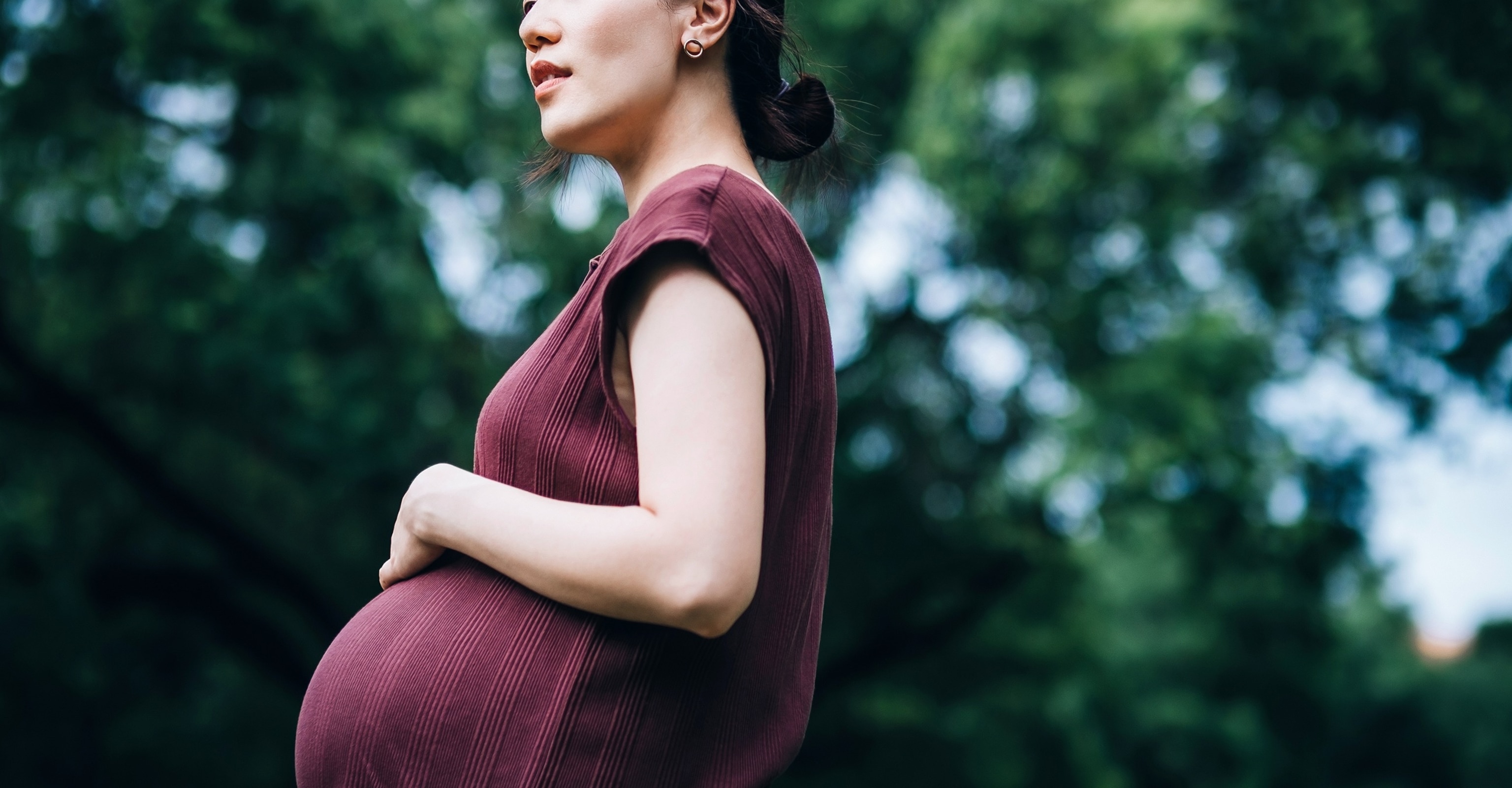PHOTO: Young Asian pregnant woman stroking her baby bump, relaxing in park. Breathing fresh air and enjoying the calmness in nature. Mother-to-be. Expecting a baby. Love and bonding. Active and healthy pregnancy lifestyle