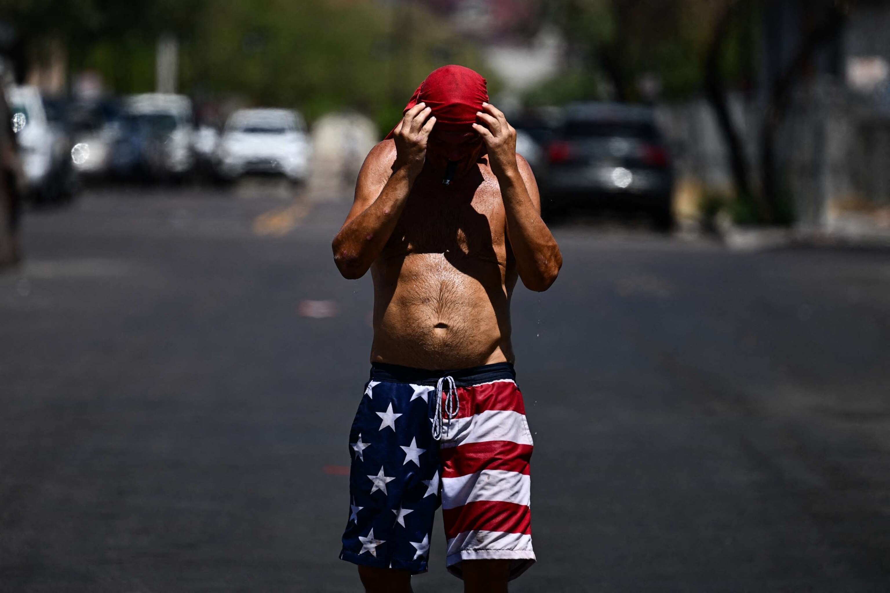 PHOTO: Water drips from a person as they grasp at their head covering while walking in the sun through "The Zone," a vast homeless encampment where hundreds of people reside, during a record heat wave in Phoenix, Arizona on July 18, 2023.