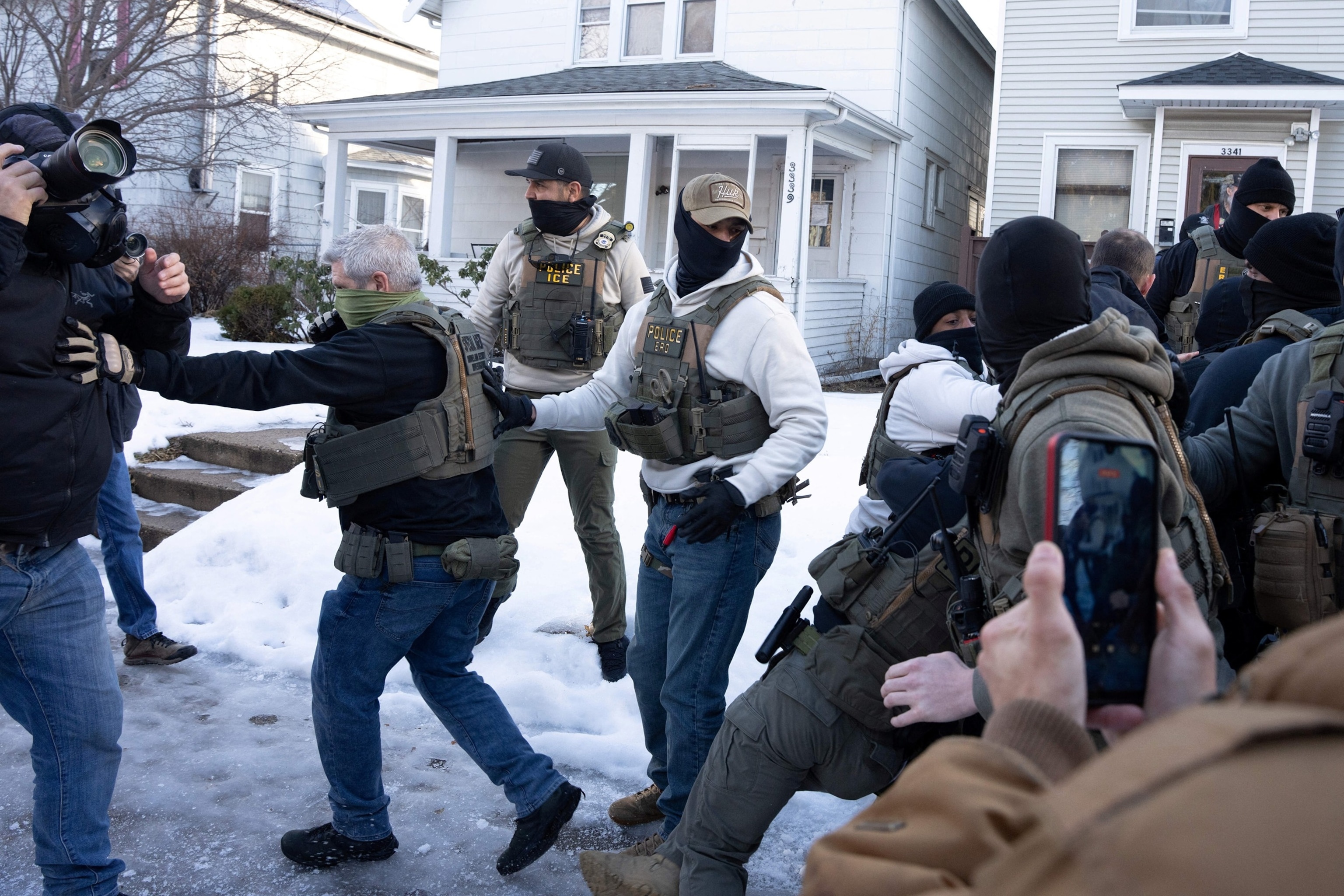 FOTO: Un agente de Homeland Securities Investigation empuja a un fotoperiodista mientras otros agentes federales abordan a un observador comunitario durante una redada de inmigración en Minneapolis, Minnesota, el 13 de enero de 2026.  