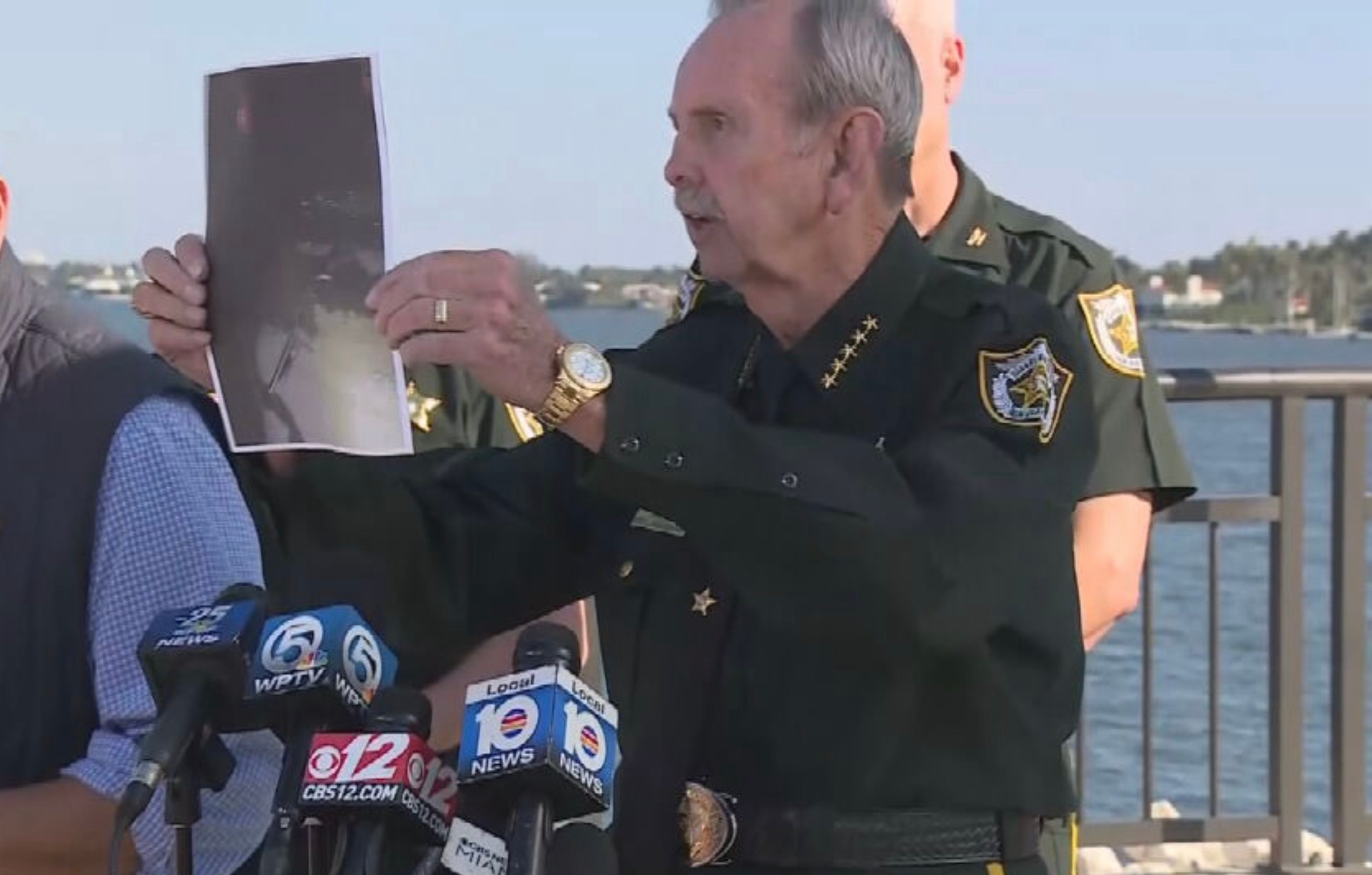 PHOTO: Palm Beach County Sheriff Ric Bradshaw holds up a photo of a gas canister and a shotgun during a news conference, February 22, 2026, which allegedly a man was carrying when he was fatally shot at President Donald Trump's Mar-a-Lago estate.