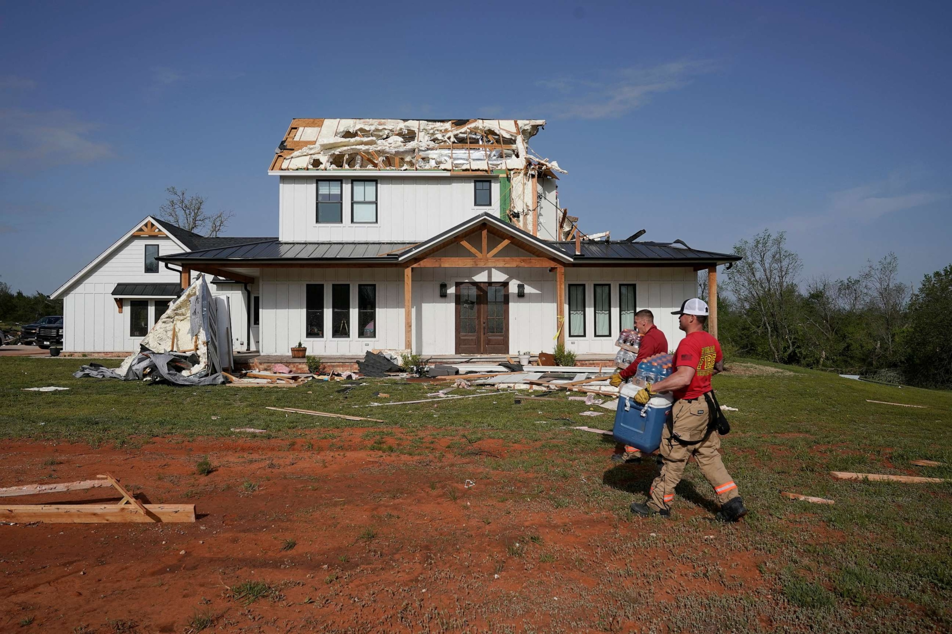 PHOTO: People walk past the damaged house destroyed during overnight tornadoes in Cole, Okla., April 20, 2023.