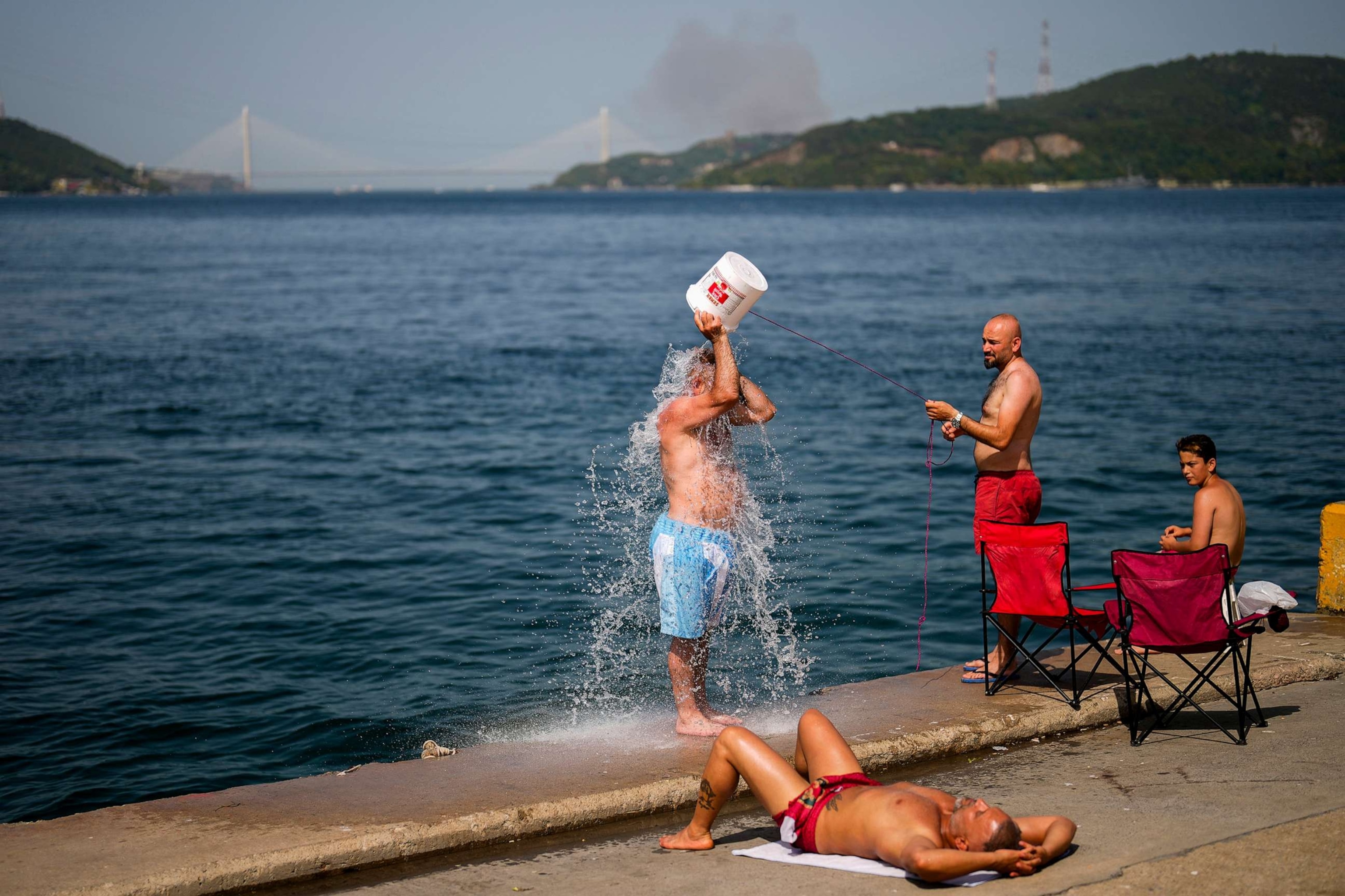 PHOTO: People cool off at the shore o the Bosphorus as a forest fire smoke rises in the background, during a hot summer day in Istanbul, Turkey, July 26, 2023.