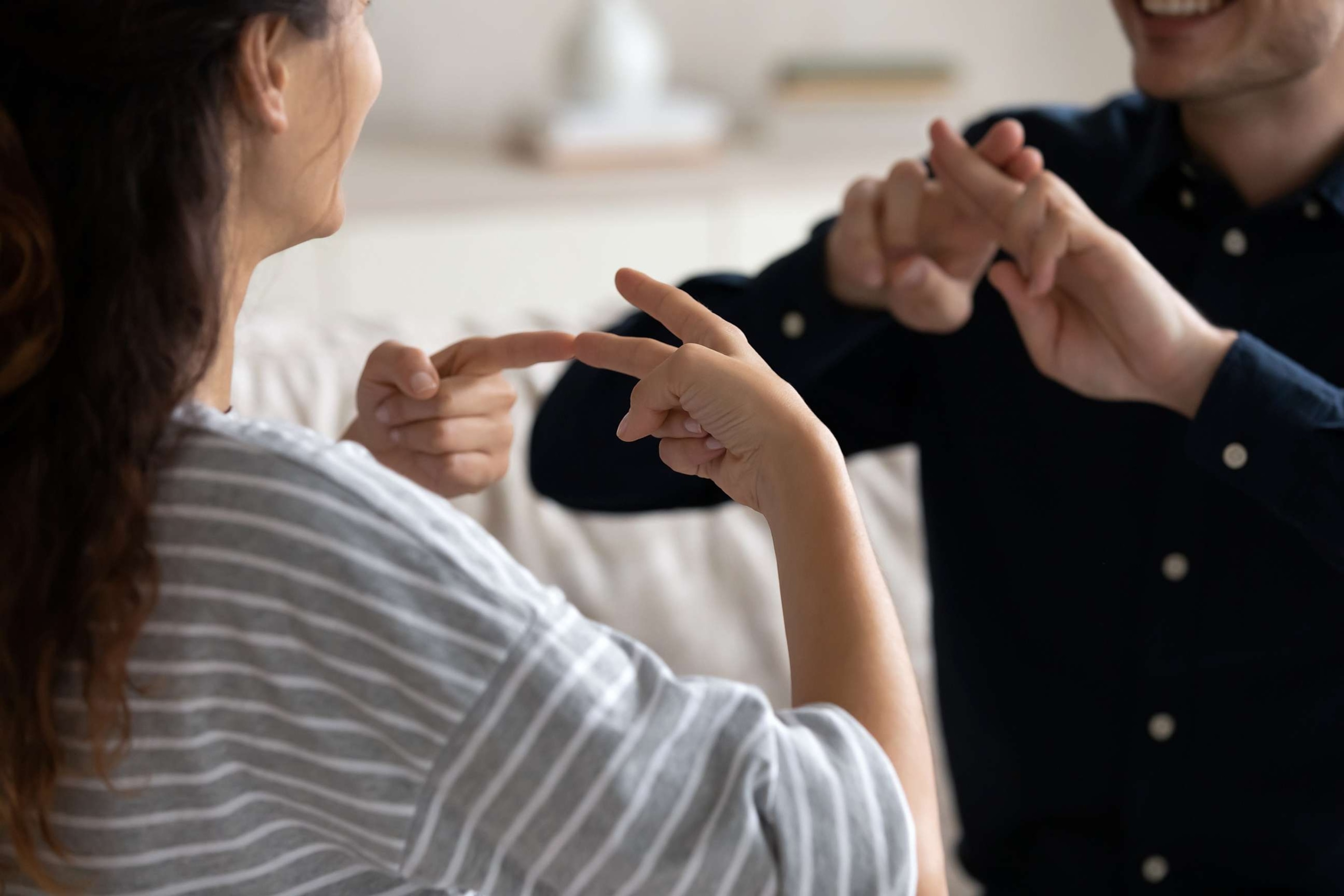 PHOTO: Young couple sit on sofa at home communicating using sign language,