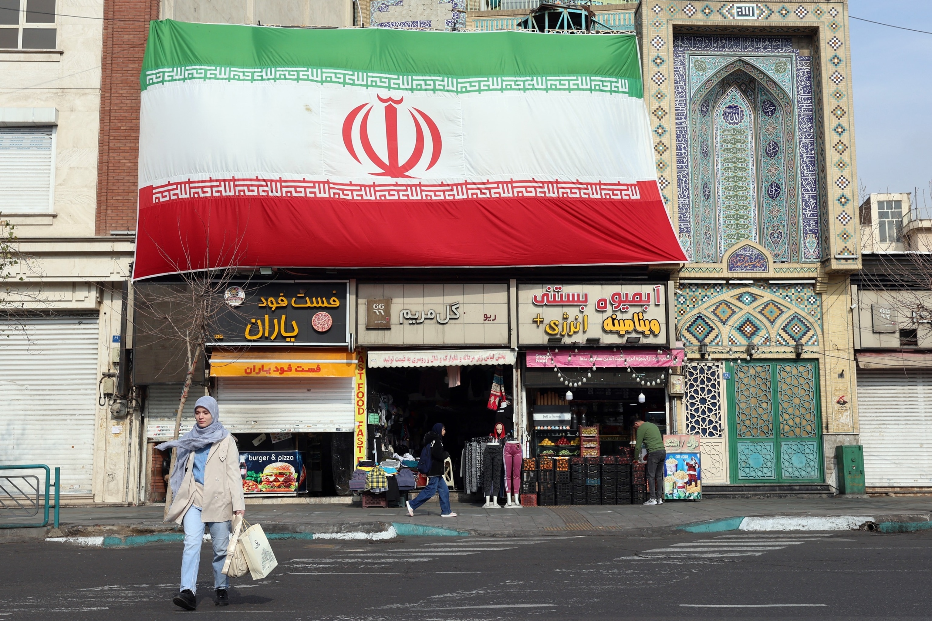 PHOTO: An Iranian woman walks past a huge national flag hanging above shops, in Tehran on Feb. 6, 2026.