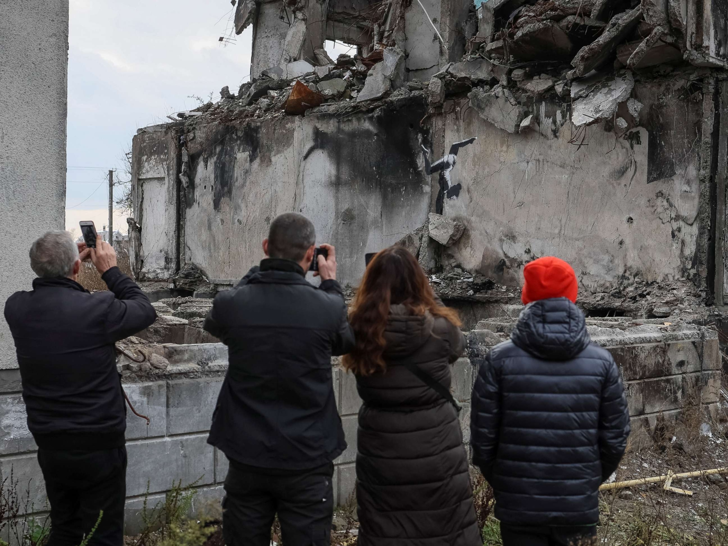 PHOTO: Local residents take photos of a work of world-renowned graffiti artist Banksy at the wall of destroyed building in the Ukrainian town of Borodianka, on Nov. 12, 2022.