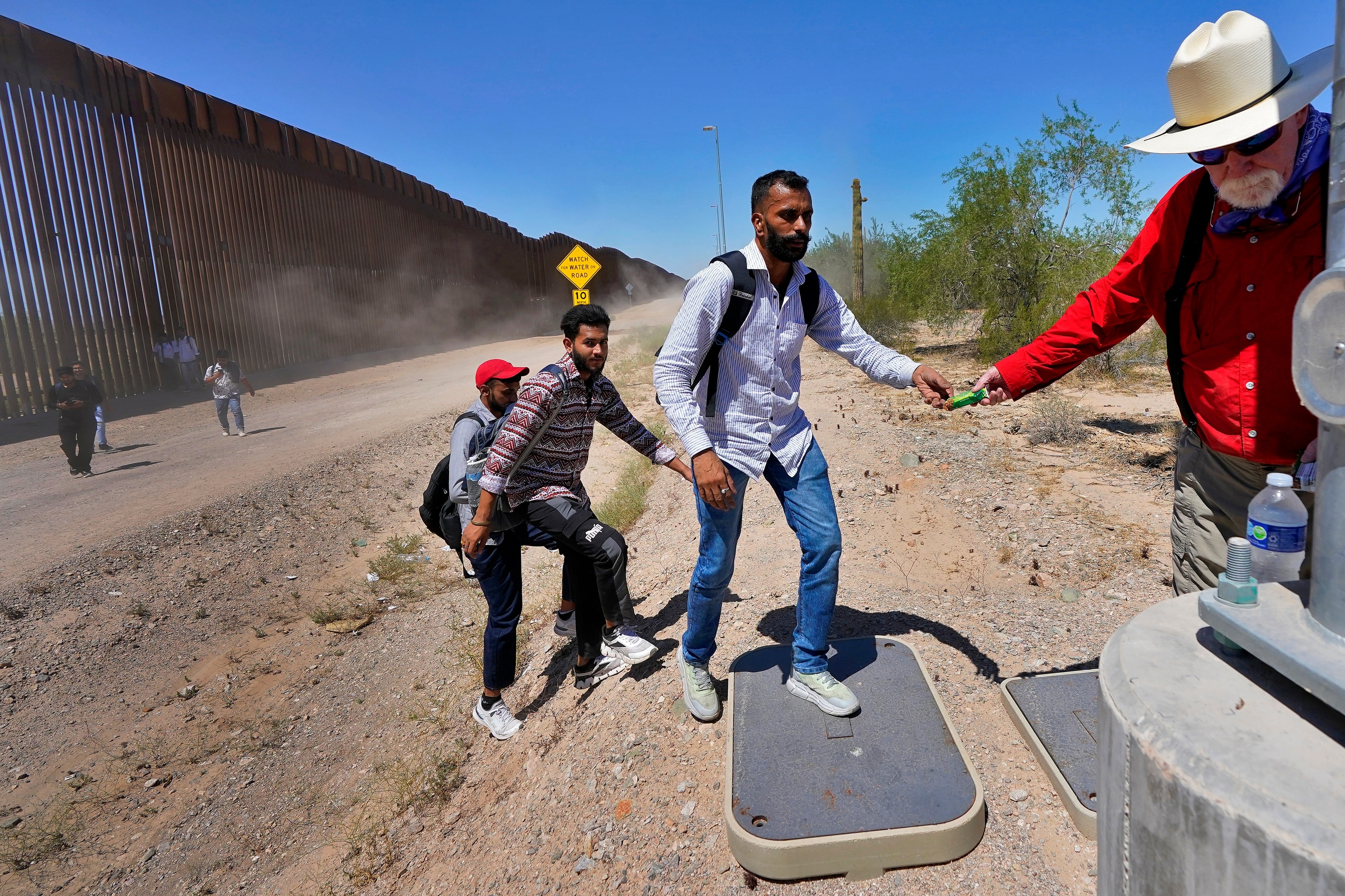 PHOTO: Tom Wingo of Samaritans Without Borders, right, gives snacks and bottles of waters to a group of migrants claiming to be from India, who just crossed the border wall, Aug. 29, 2023, in Organ Pipe Cactus National Monument near Lukeville, Ariz.