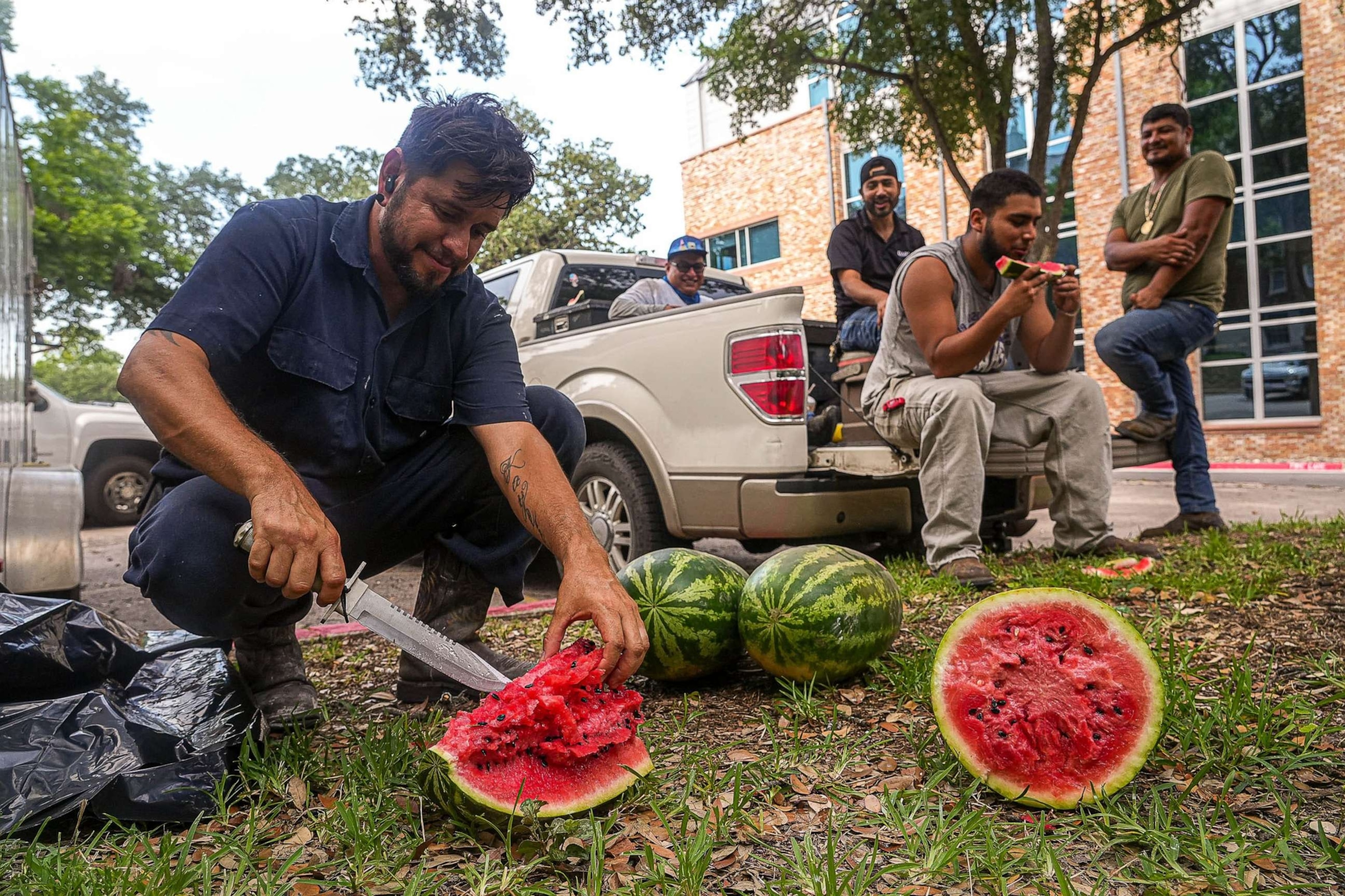 PHOTO: Junior Chavez, a painter for Dart Construction, slices watermelon for his coworkers while taking a break from painting window frames on the Scottish Rite Dormitory, June 19, 2023, in Austin, Texas.