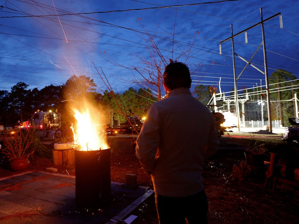 PHOTO: Gerardo Anicero warms himself in front of a makeshift fire as he watches Duke Energy personnel work to restore power at a crippled electrical substation in Carthage, N.C., on Dec. 4, 2022. 