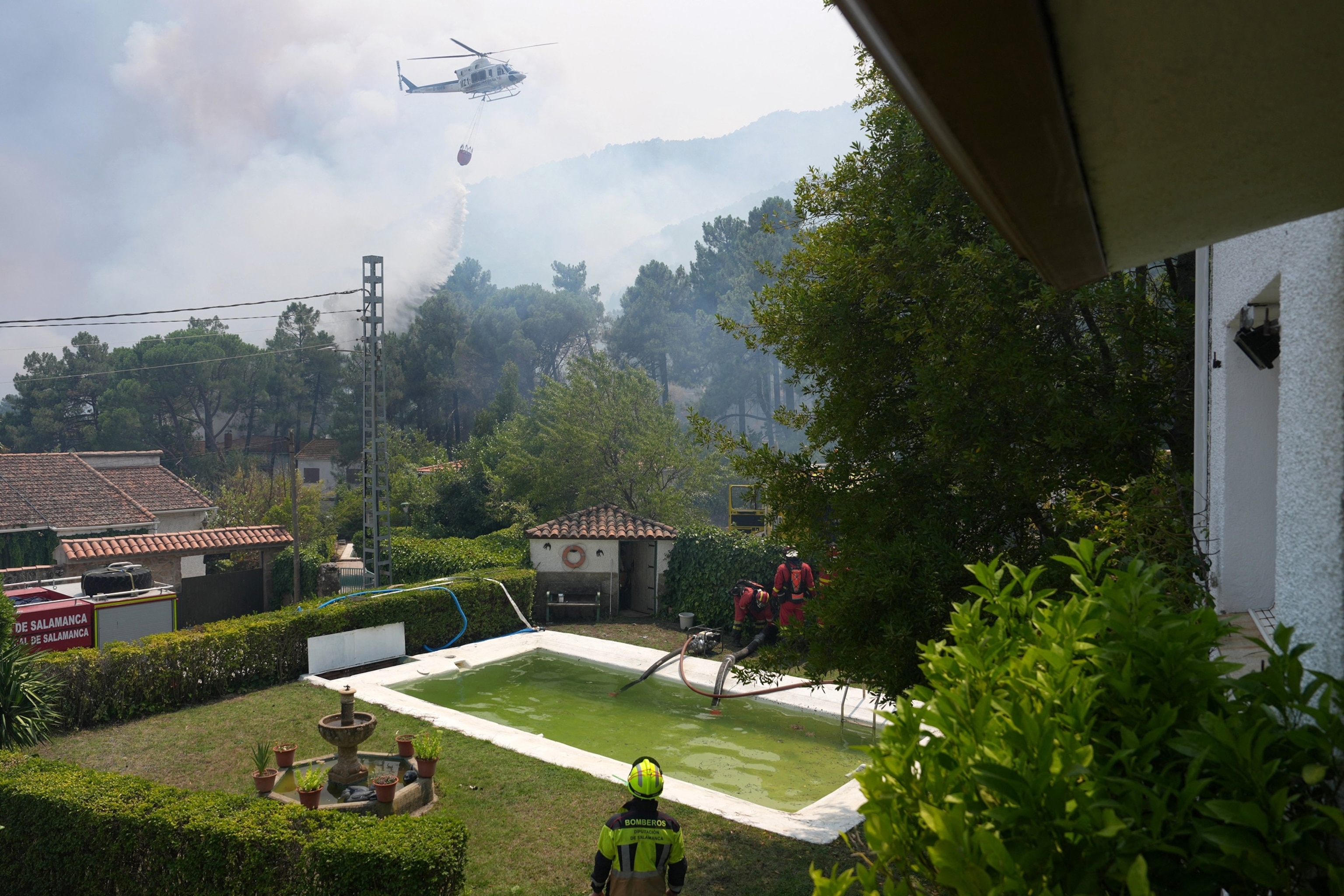 PHOTO: A firefighter helicopter dumps water as firefighters collect water from a swimmming pool while battling a fire surrounding La Atalaya residential area in El Tiemblo, Spain, 80 kms west of Madrid, on July 25, 2026.