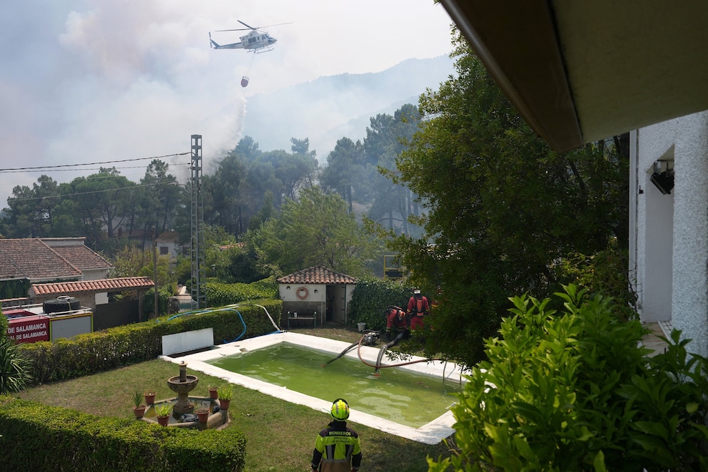 PHOTO: A firefighter helicopter dumps water as firefighters collect water from a swimmming pool while battling a fire surrounding La Atalaya residential area in El Tiemblo, Spain, 80 kms west of Madrid, on July 25, 2026.