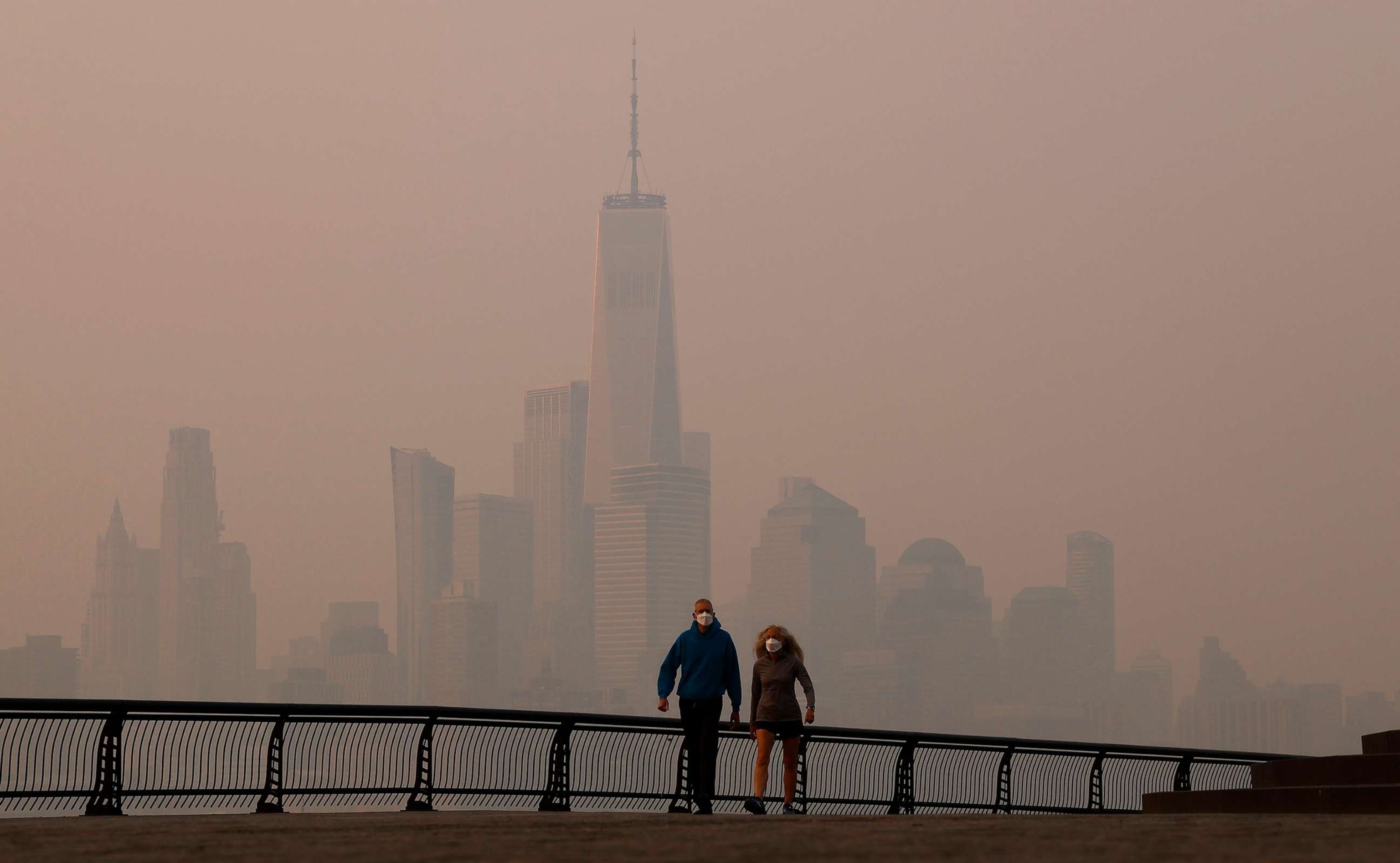 PHOTO: People wearing masks walk along the Hudson River as smoke shrouds the skyline of lower Manhattan and One World Trade Center as the sun rises in New York, June 8, 2023, as seen from Hoboken, N.J.