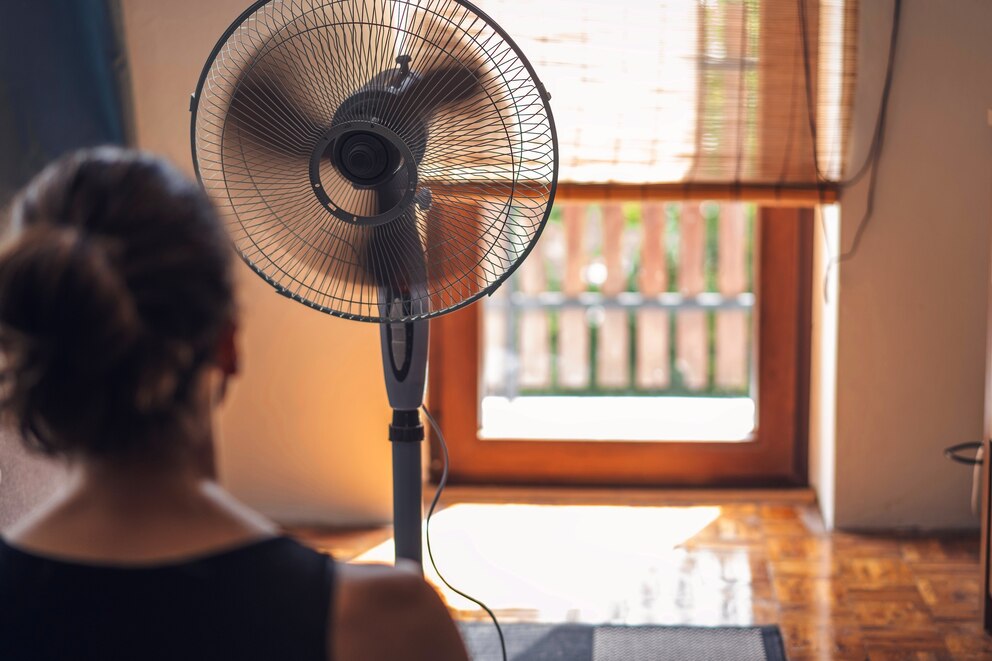 PHOTO: Young woman sitting at home in front of a fan escaping from the summer heat.