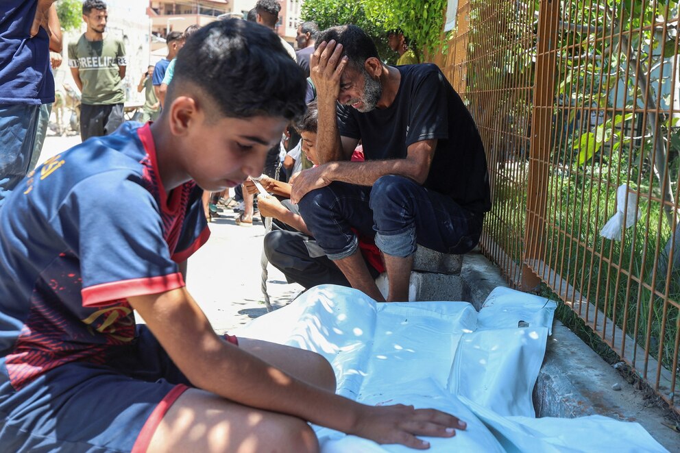 PHOTO: A Palestinian man from the Katoo family, with his son, mourns beside the body of his other son, who was killed by Israeli fire while seeking aid near a distribution point in Rafah, at Nasser Hospital in the southern Gaza Strip, July 12, 2025. 