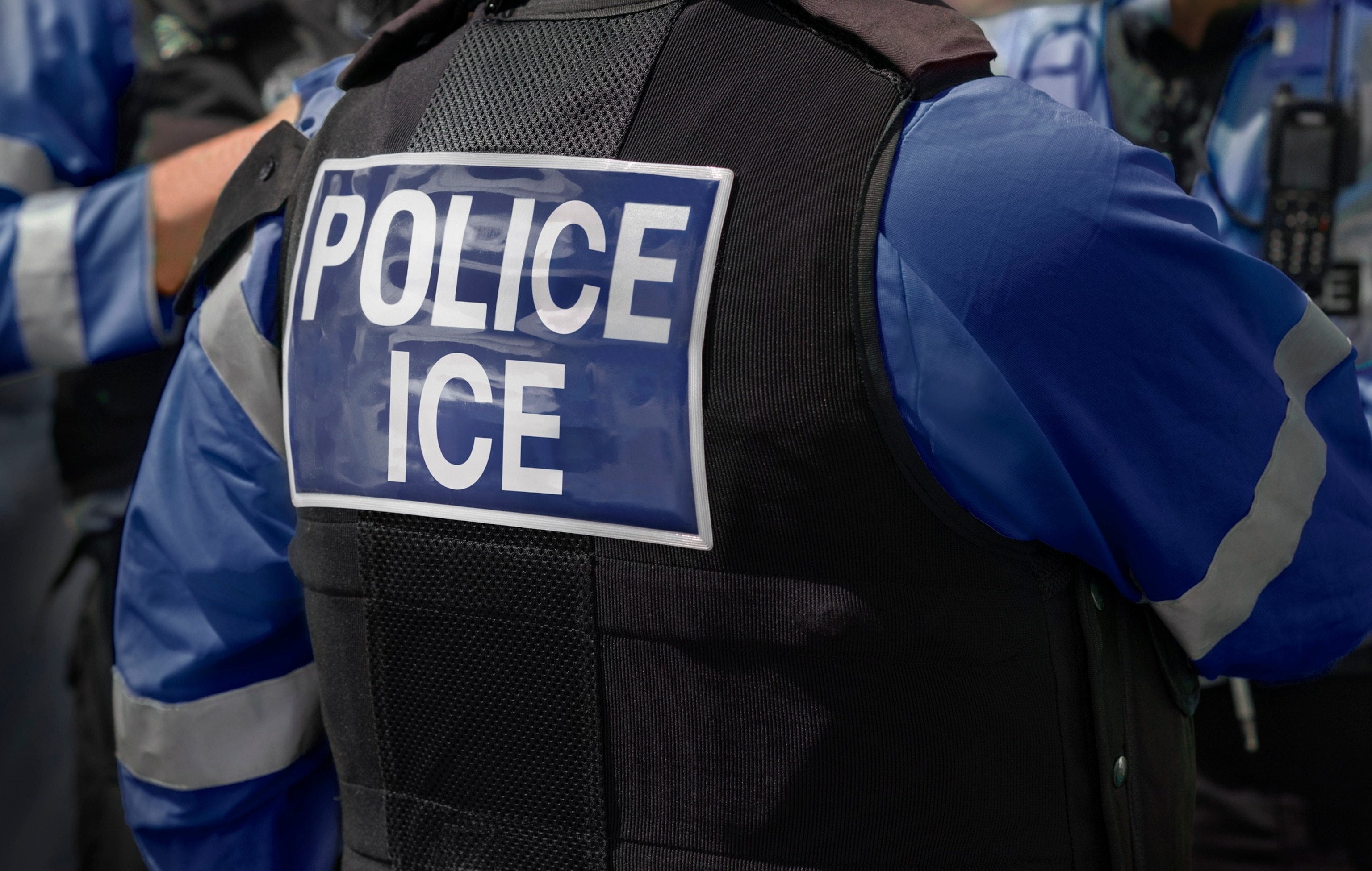 PHOTO: Ice Police agents - Immigration and Customs Enforcement. Close-up of POLICE ICE marking on the back of worn by a trio of DHS police officers at the scene of an incident.