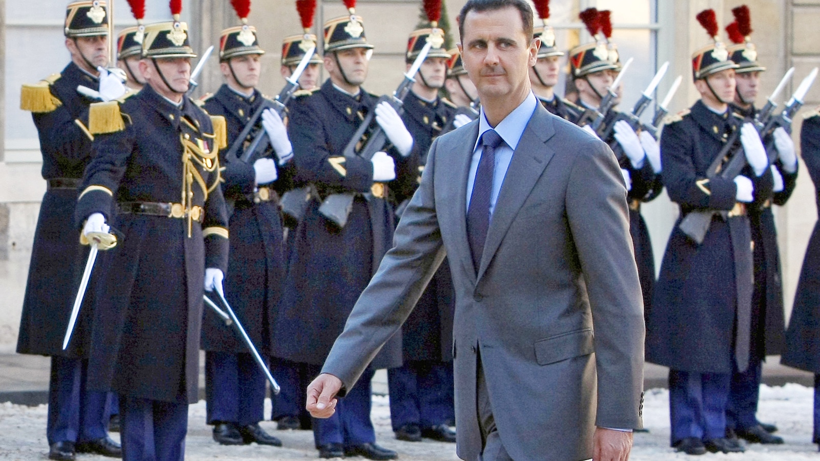A man in a suit stands in front of a line of uniformed guards.