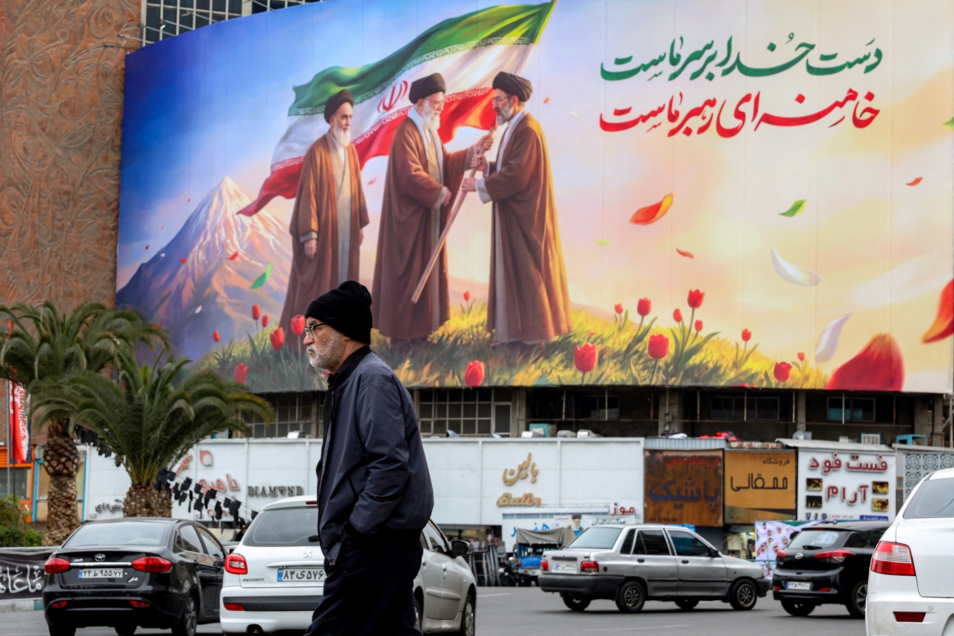 PHOTO: A man walks near a banner displayed at Valiasr Square in central Tehran on March 10, 2026, depicting Iran's late supreme leaders Ayatollah Ruhollah Khomeini and Ayatollah Ali Khamenei and new supreme leader Mojtaba Khamenei.