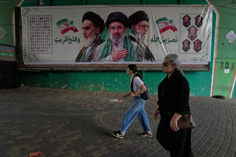 PHOTO: Women walk past a banner showing portraits of Ayatollah Ruhollah Khomeini (L), Supreme Leader Ayatollah Mojtaba Khamenei (C), and the late Supreme Leader Ayatollah Ali Khamenei, under a bridge in northern Tehran, Iran, on Aug. 2, 2026.