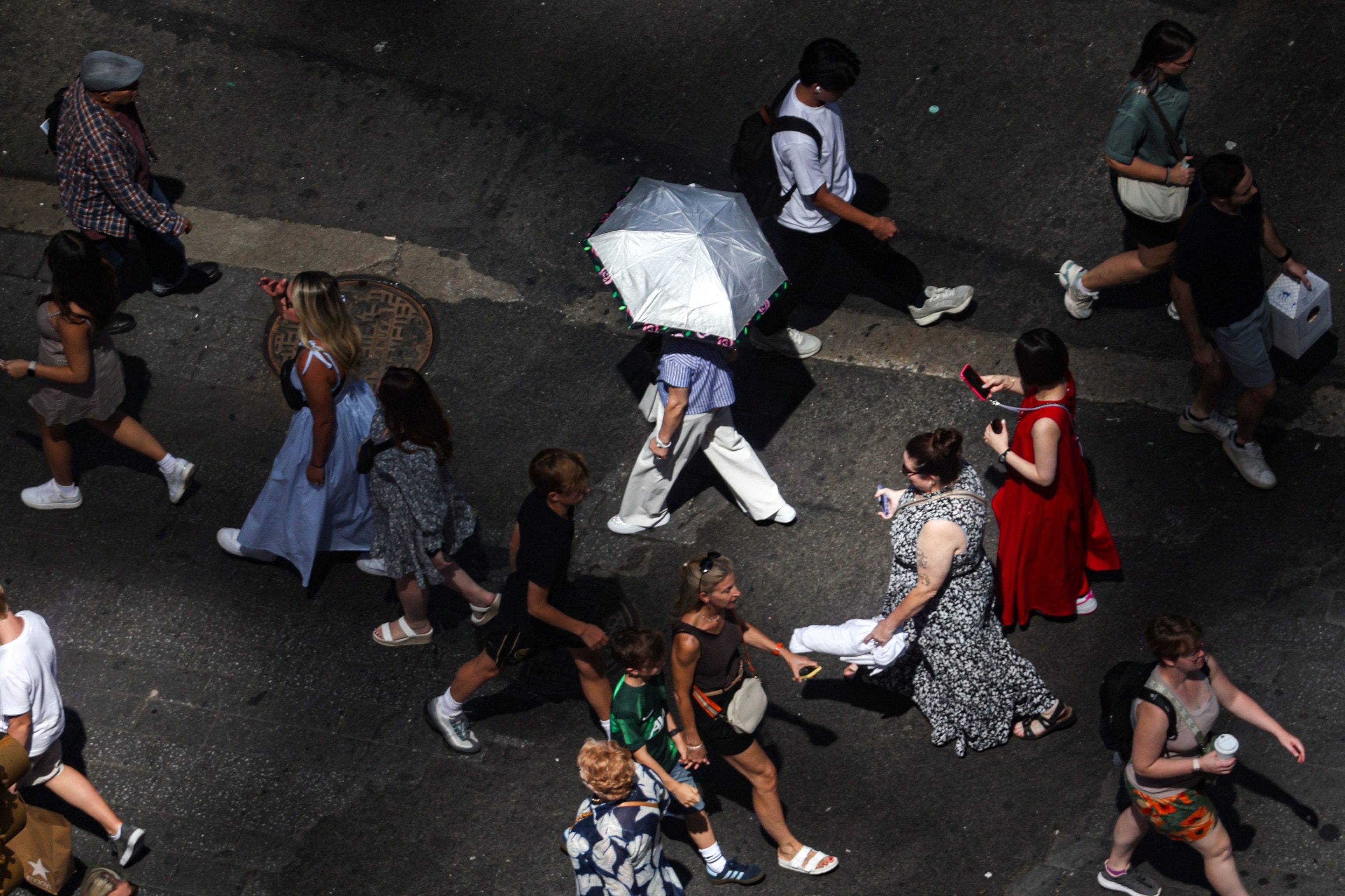 PHOTO: Pedestrians, including a person holding an umbrella to block UV rays, walk through Times Square in New York