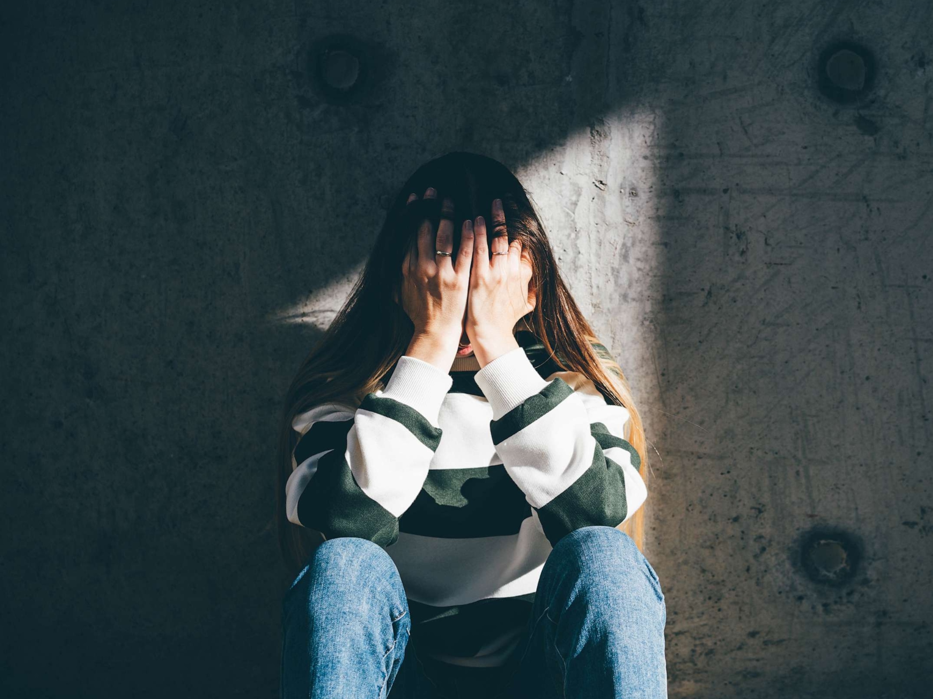 PHOTO: In an undated stock photo, a woman sits against a wall with her head in her hands.