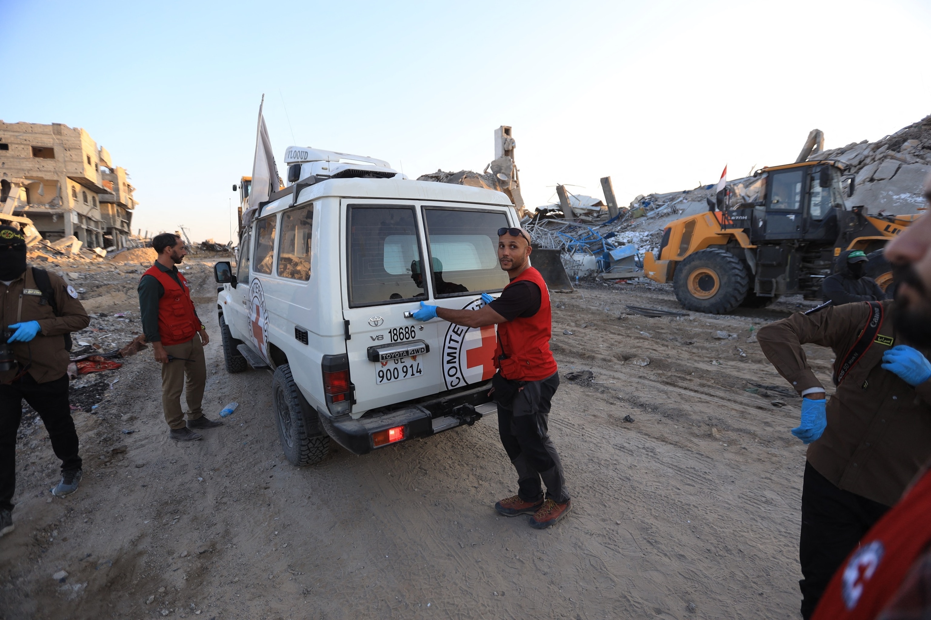 PHOTO: The Red Cross stand next to a vehicle is parked next to rubble as Islamic Jihad and Hamas militants transport a white body bag believed to carry the remains of an Israeli hostage in the town of Beit Lahia in the northern Gaza Strip on Dec. 3, 2025.