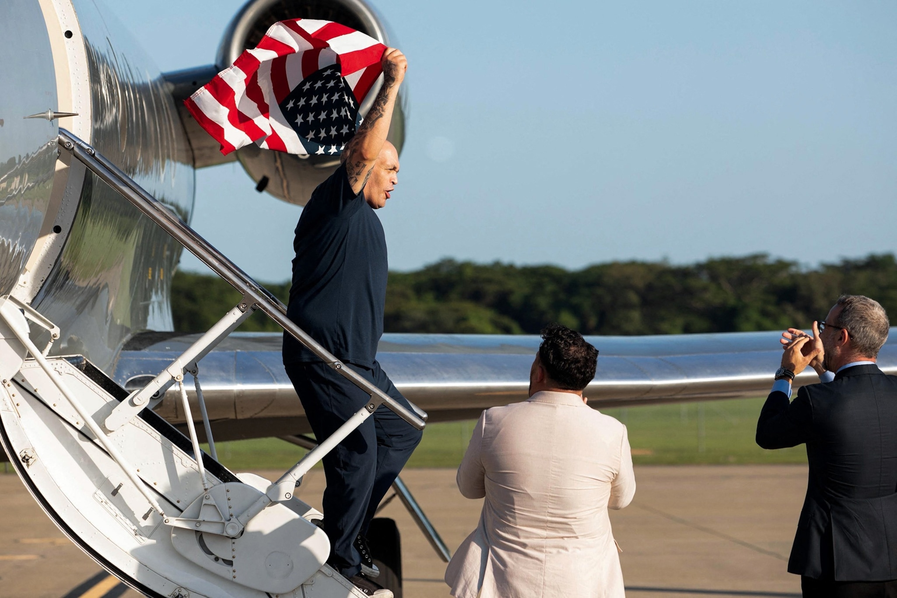 PHOTO: One of the 10 US citizens exchanged between the US government and the Venezuelan government waves a US flag upon arrival  at the San Oscar Romero International Airport in San Luis Talpa, El Salvador, on July 18, 2025. 
