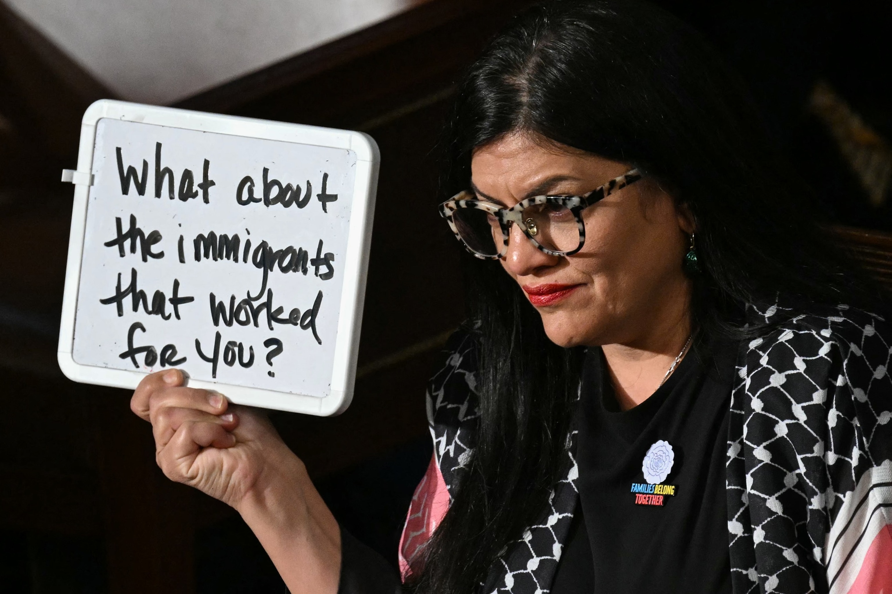 PHOTO: Representative Tlaib (D-MI) holds up a white board reading "What about the immigrants that worked for you?" as President Trump speaks during an address to a joint session of Congress in Washington, DC, on March 4, 2025.
