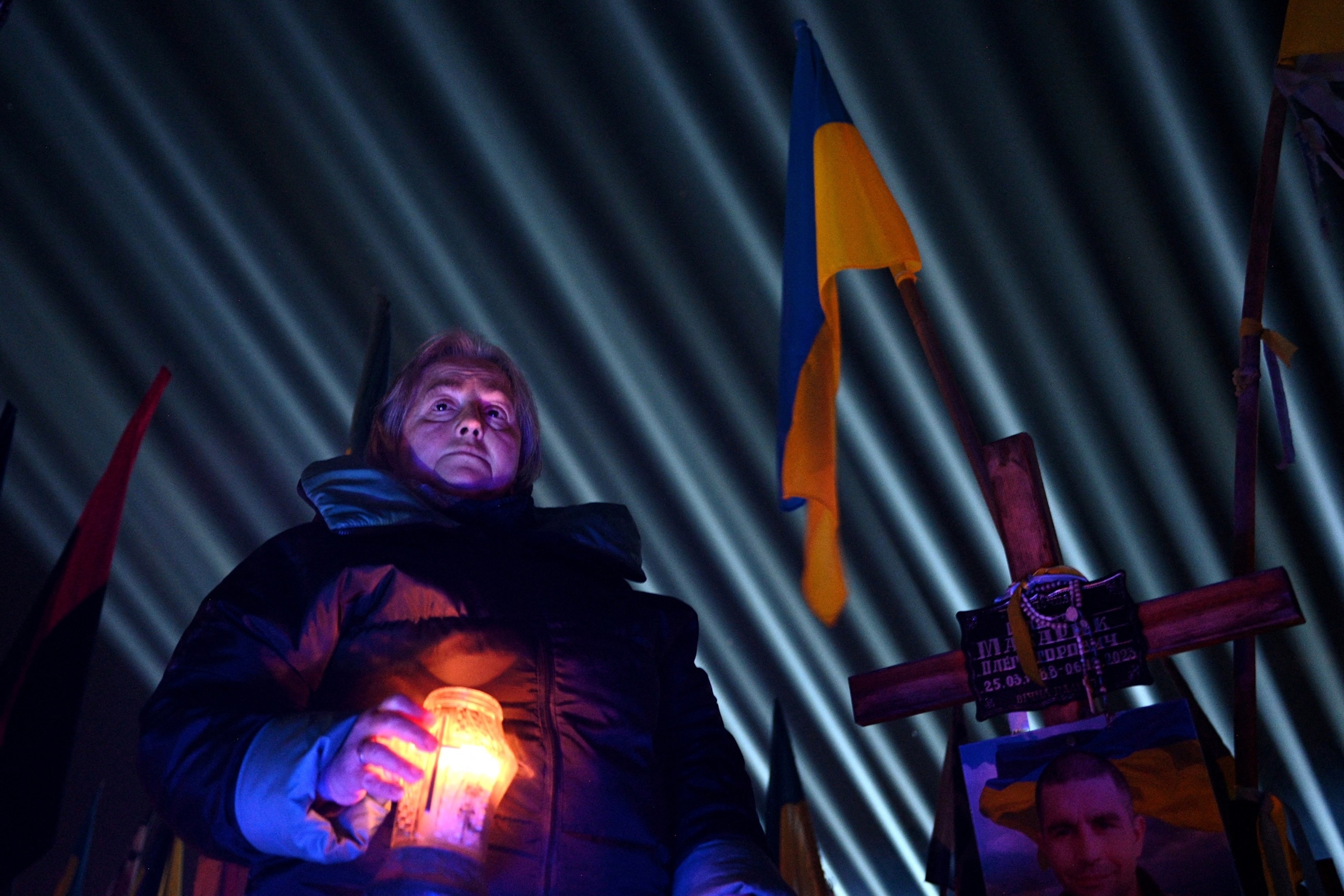 PHOTO: A woman holds a candle as a symbolic illumination entitled "Rays of Memory" is projected over the graves of Ukrainian soldiers who died in the war with Russia, at Lychakiv Military Cemetery in Lviv on Feb. 23, 2026.