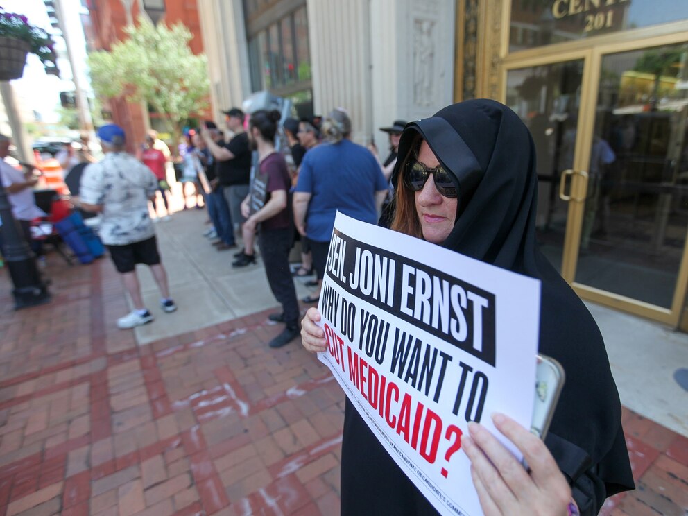 PHOTO: Lesa Hadley of Bettendorf, Iowa stands  outside the office of U.S. Sen. Joni Ernst (R-IA) wearing a cloak as part of a mock funeral to protest against proposed Medicaid cuts on June 23, 2025  in Davenport, Iowa.
