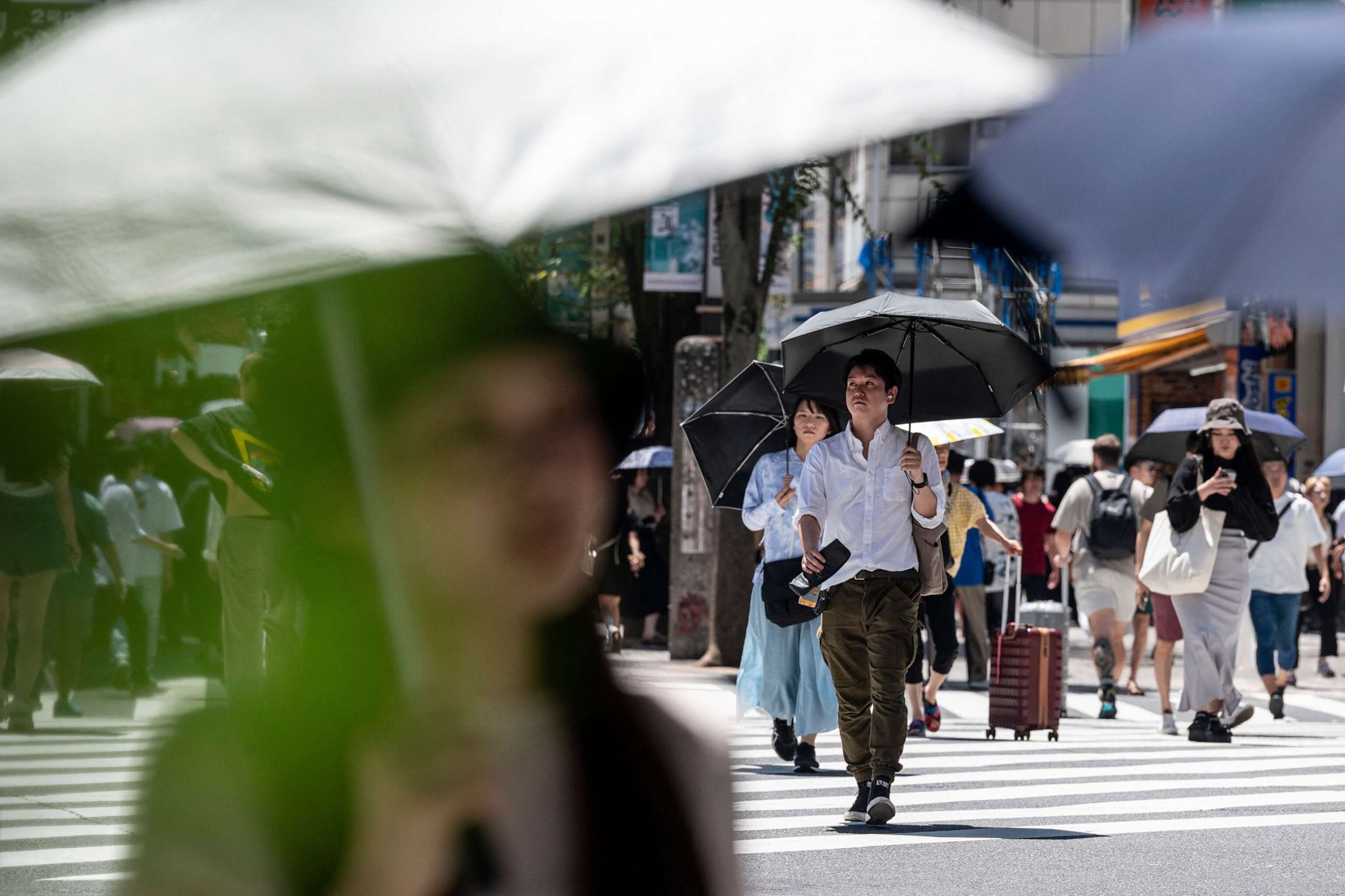 PHOTO: Men and women use umbrellas and parasols to seek relief from the heat while crossing a street in Tokyo, July 30, 2023.