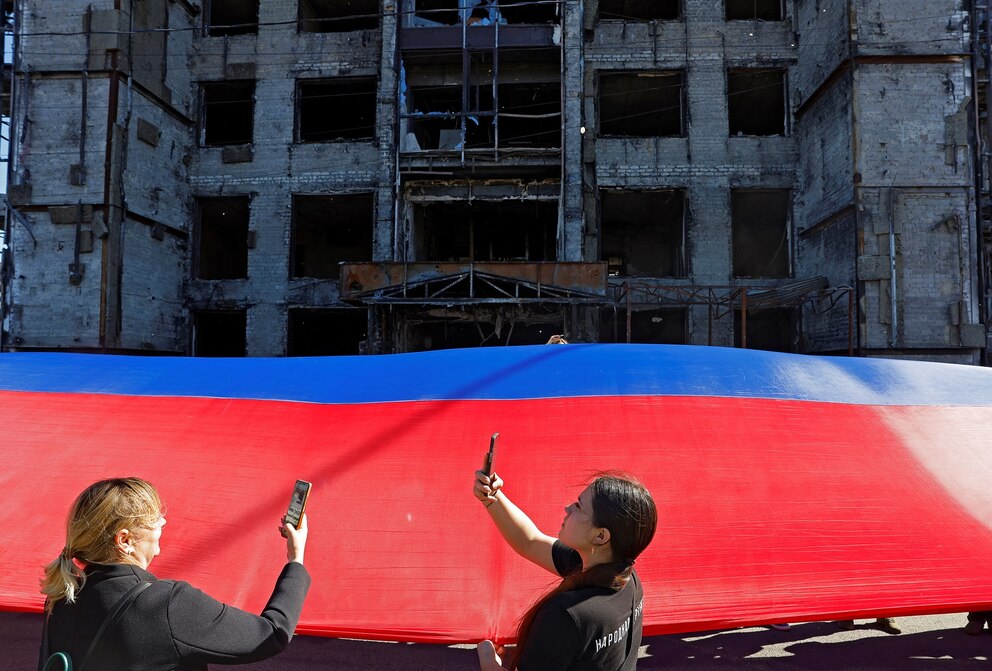 PHOTO: Volunteers take pictures while holding a giant flag of the Donetsk People's Republic region during a ceremony marking the anniversary of the taking control of the city by Russia, in Mariupol, a Russian-controlled city of Ukraine, May 18, 2025.