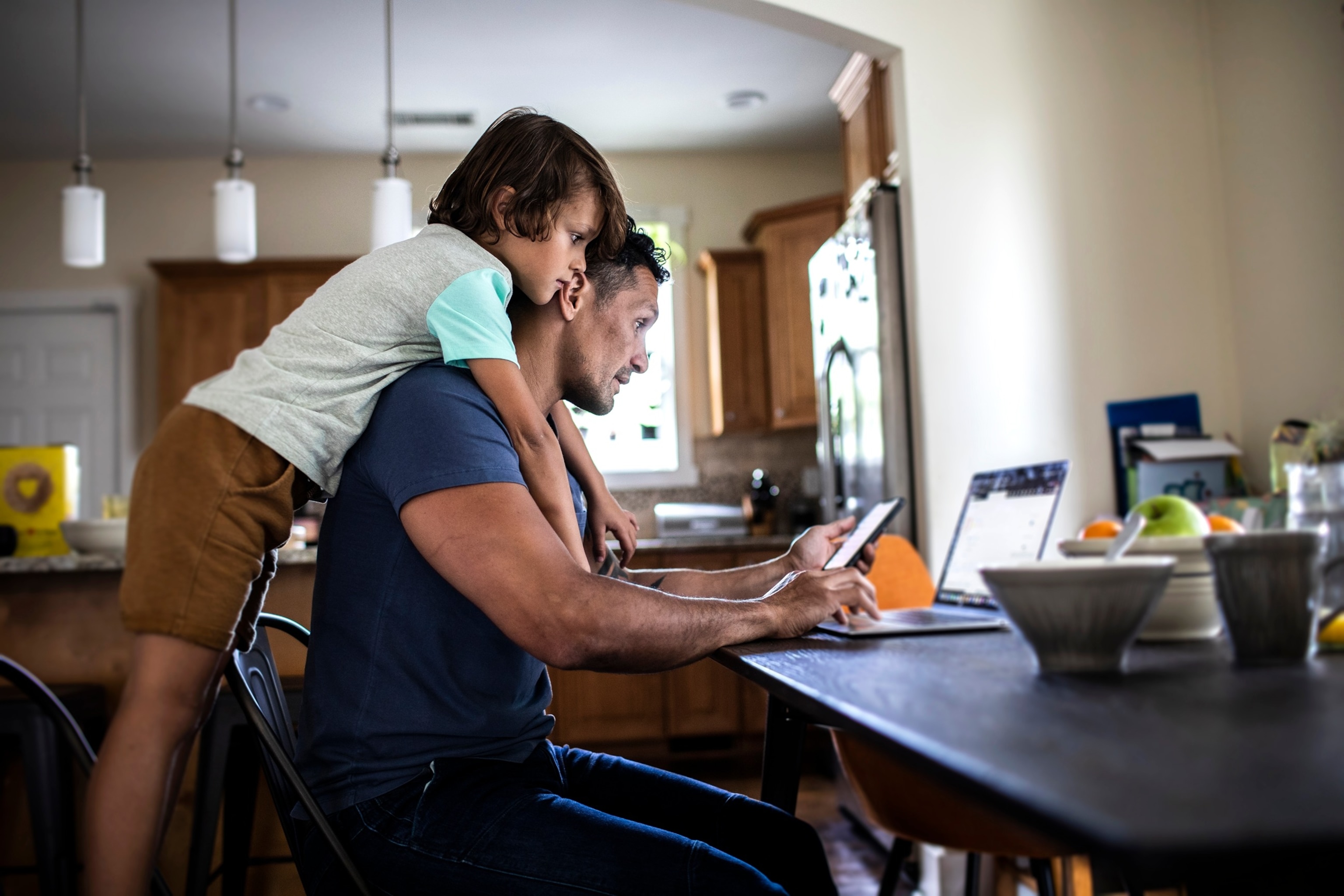 A father uses a laptop with his young son looking over his shoulder.